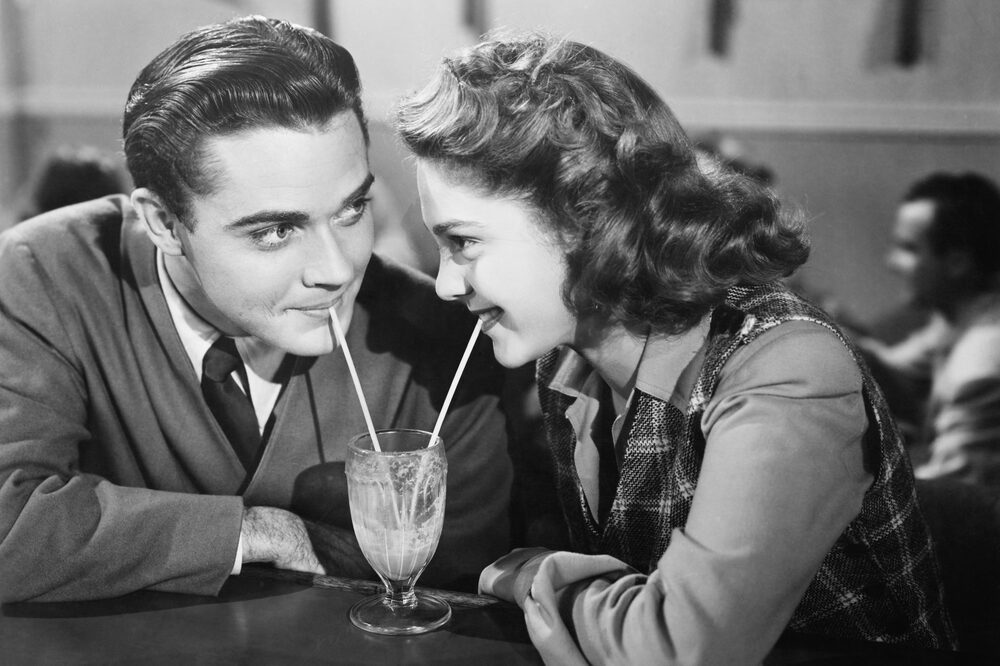 Couple in a restaurant looking at each other and sharing a milk shake with two straws