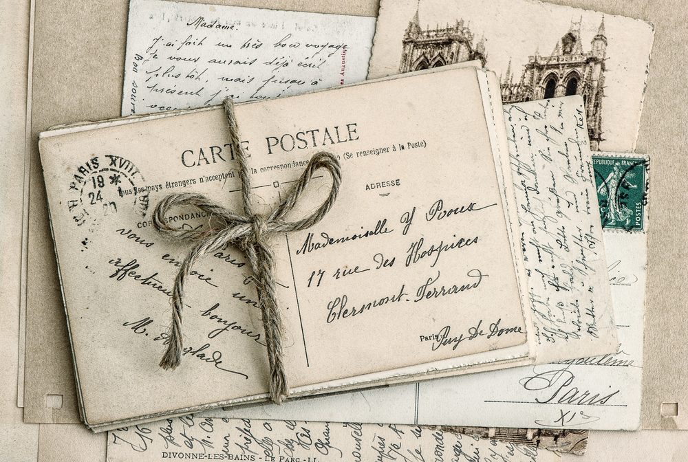 Postcard bundle tied with string, displaying cursive writing and addressing "Mademoiselle Y. Rous" in a vintage, nostalgic setting with other postcards and stamps.