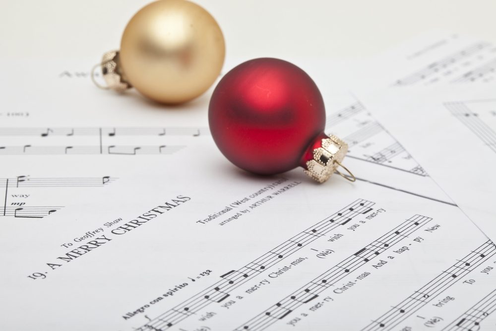 Ornaments rest on Christmas sheet music, featuring red and gold spheres, surrounded by musical notes and lyrics, creating a festive holiday atmosphere.