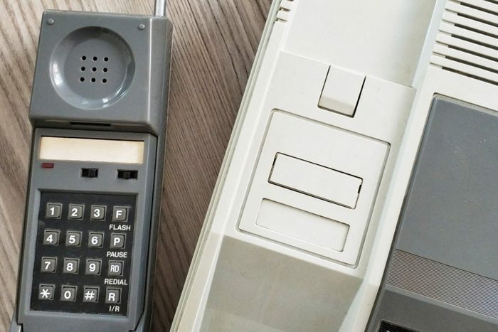 Retro cordless phone with keypad, resting on a wooden surface, beside its base station with slots and buttons.
