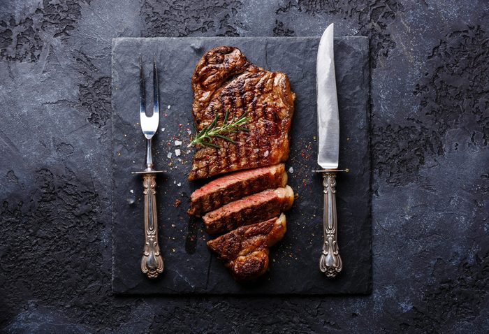 Sliced grilled meat barbecue steak Striploin with knife and fork carving set on black stone slate