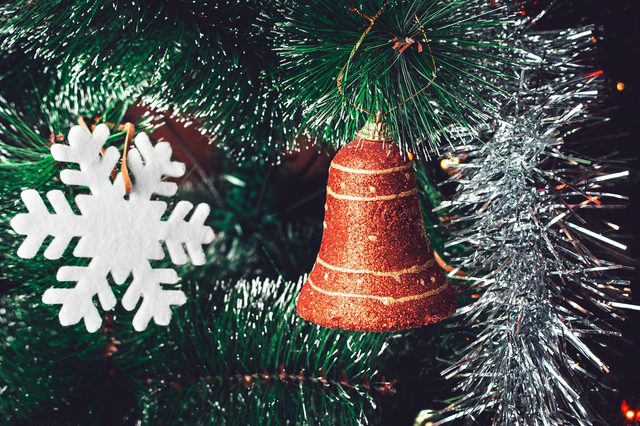 A glittery red bell hangs on a Christmas tree adorned with silver tinsel and a white felt snowflake.