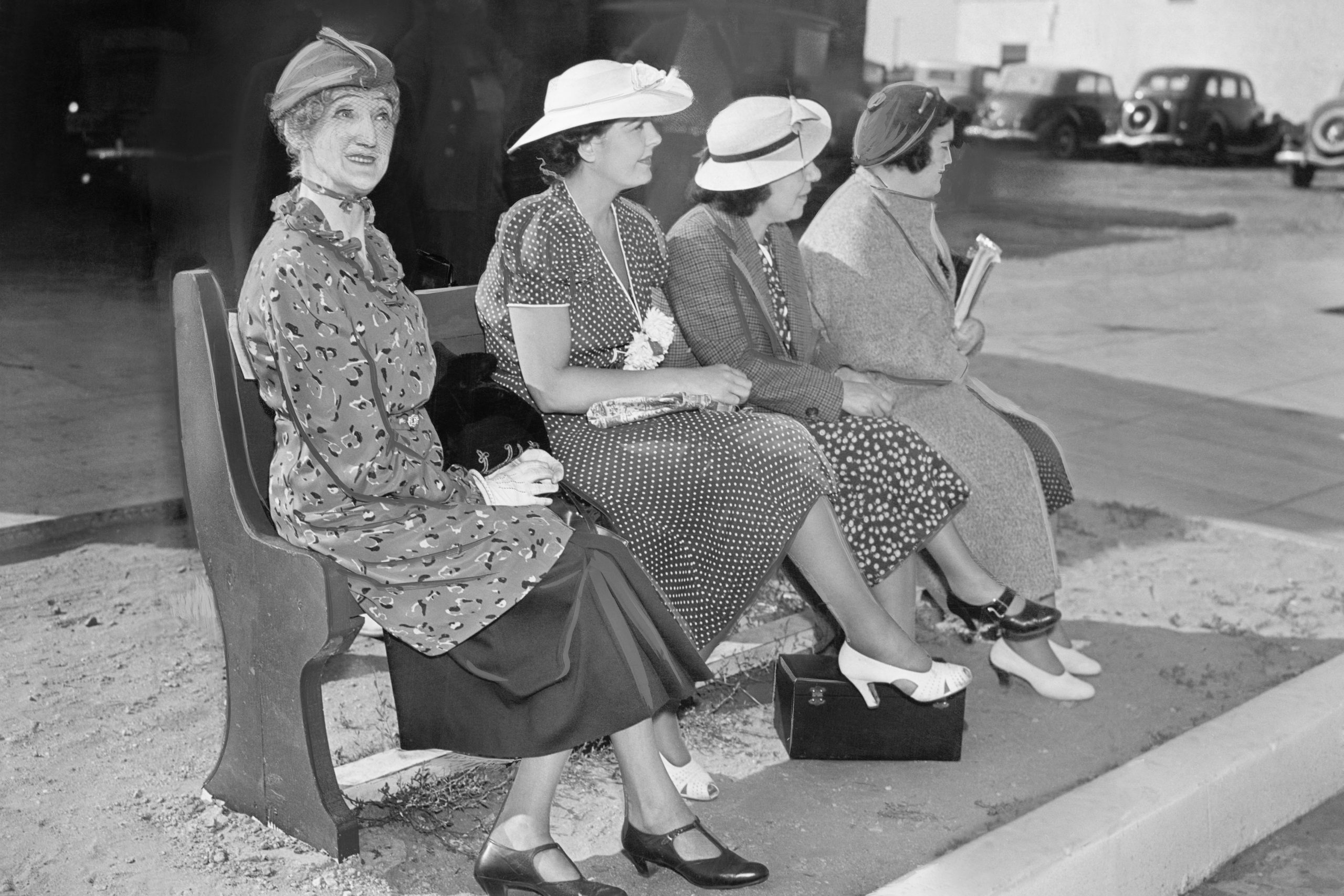 Four women sitting on a bench waiting for the bus
