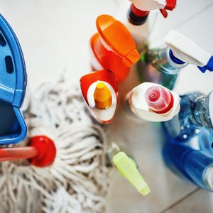 Cleaning products are arranged with spray bottles surrounding a mop and bucket on a tiled floor.