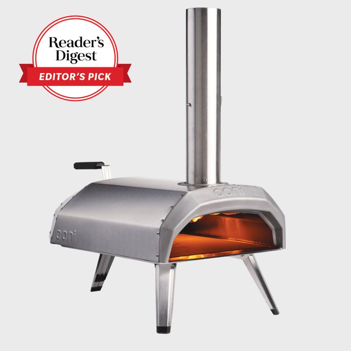 A stainless-steel pizza oven emits an orange glow, standing against a plain background; marked with â€œReaderâ€™s Digest Editorâ€™s Pickâ€ in red and white text.