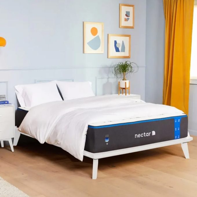 Bed sits neatly in a bright room, surrounded by abstract wall art and yellow curtains, with a 