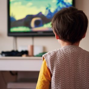 Child watches a colorful cartoon on a wall-mounted television in a cozy living room.