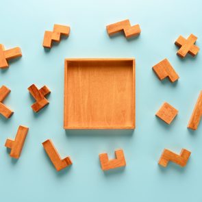 Wooden puzzle pieces surround an empty square wooden tray on a light blue background.
