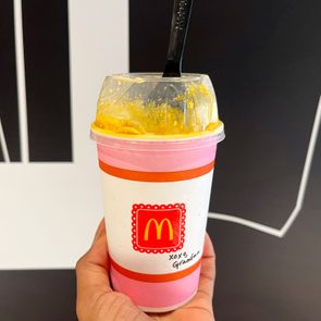Hand holds McDonald's dessert cup with spoon, yellow ice cream inside, against a black and white background. Text on cup: 