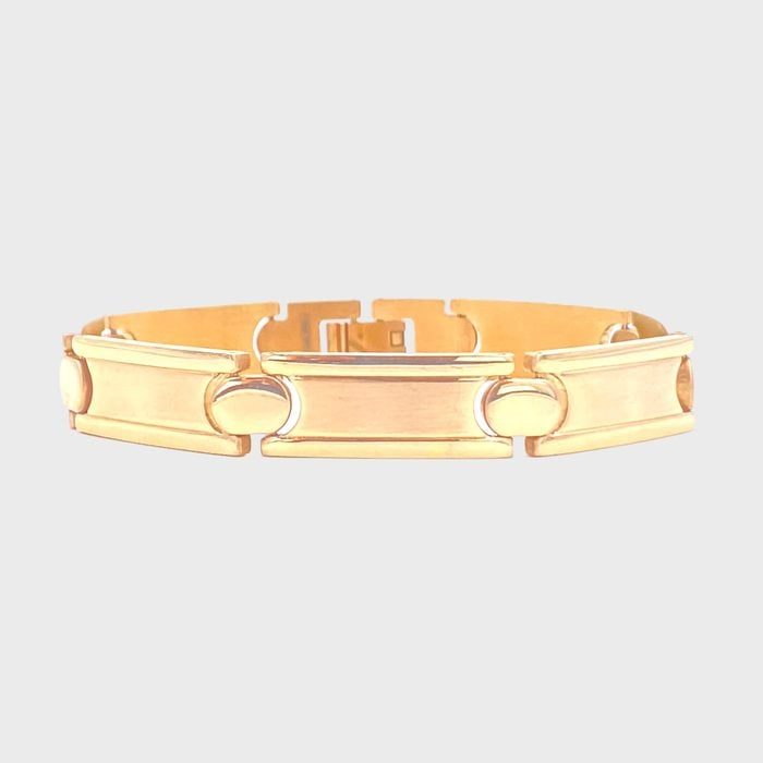 Gold bracelet featuring rectangular links with circular cutouts, resting on a plain white background.