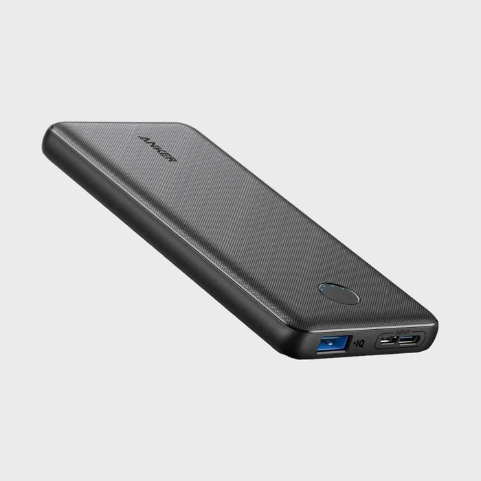 Black power bank rests diagonally; features USB ports and LED indicator; set against a plain gray background.