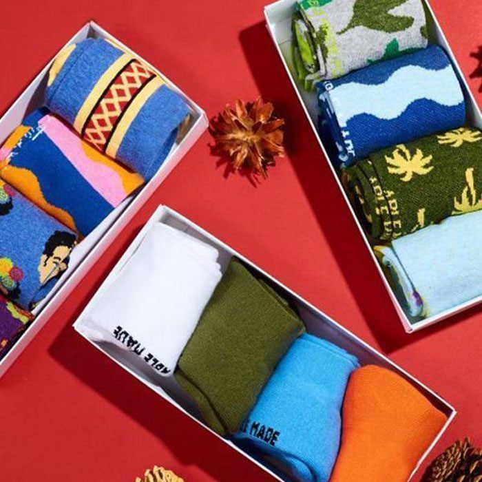 Boxed socks display vibrant designs, resting on a red surface, surrounded by decorative pine cones.
