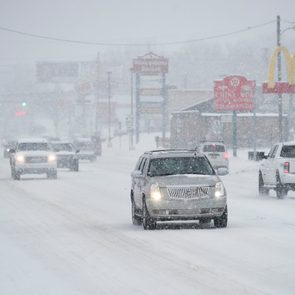 Cars drive on a snowy road with fast food signs in the background