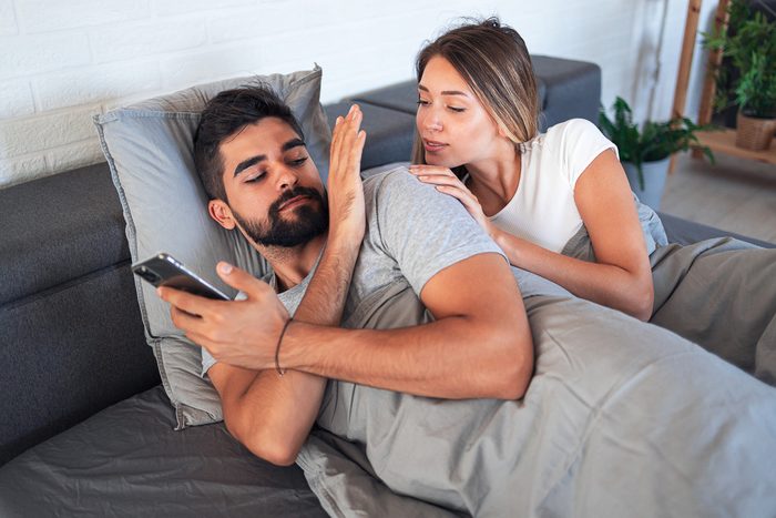 couple in bed. man is not letting woman see his phone.