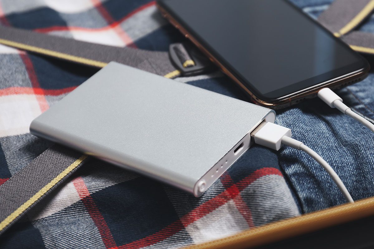 Smartphone charging with power bank, passport and clothes in open suitcase, closeup