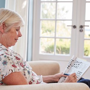 Senior Woman Sitting In Armchair Doing  A Crossword At Home