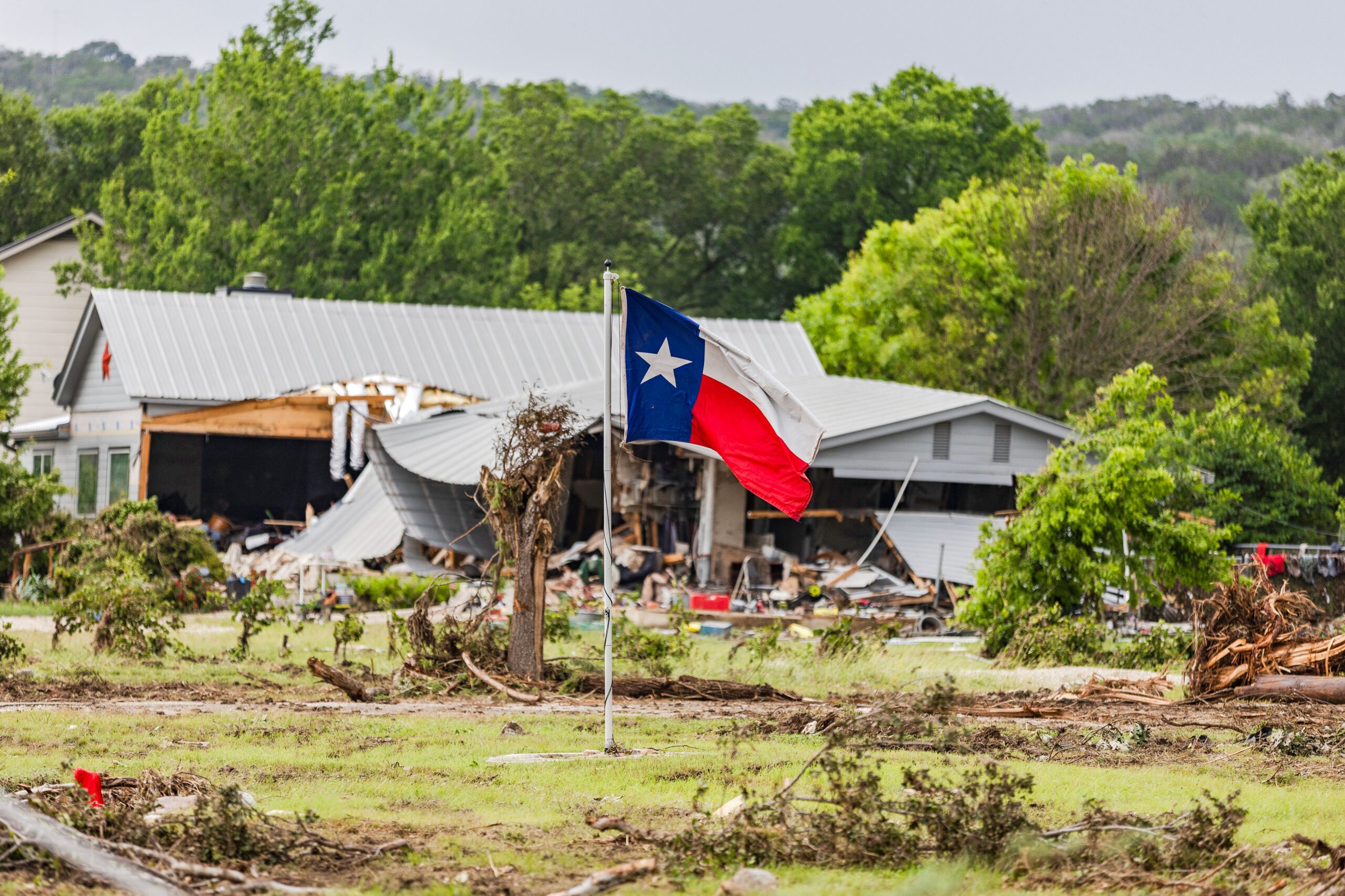 A Texas state flag flies in a yard filled with debris