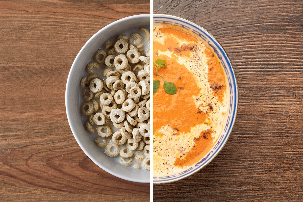 A bowl split in half: the left side contains cereal rings with milk, and the right side contains a creamy soup with herbs, both on a wooden table.